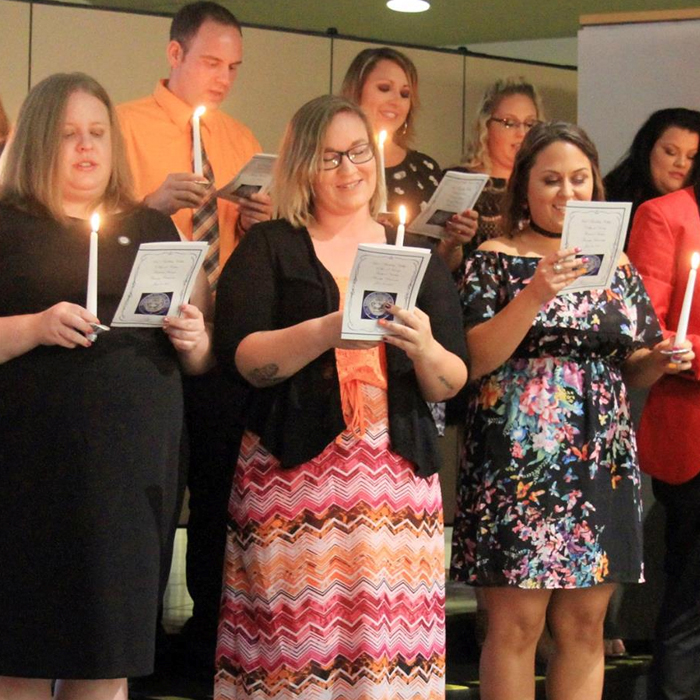 a group of students holding a candle reading from a paper at nursing graduation.