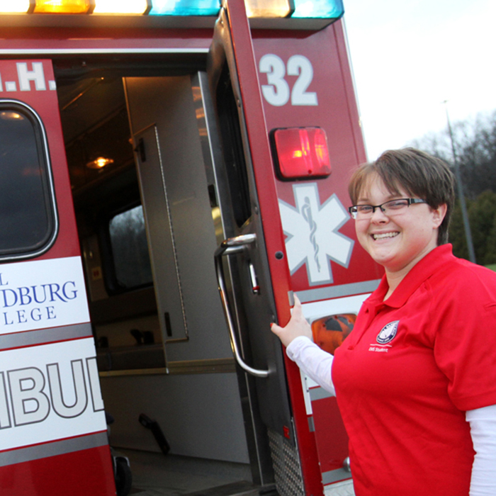 a smiling woman holding the door of an ambulance open.