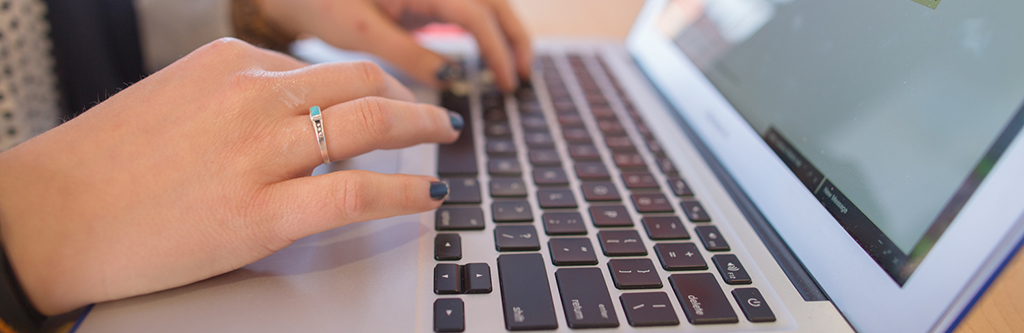 female hand with a ring on it typing on a laptop sitting on a table.