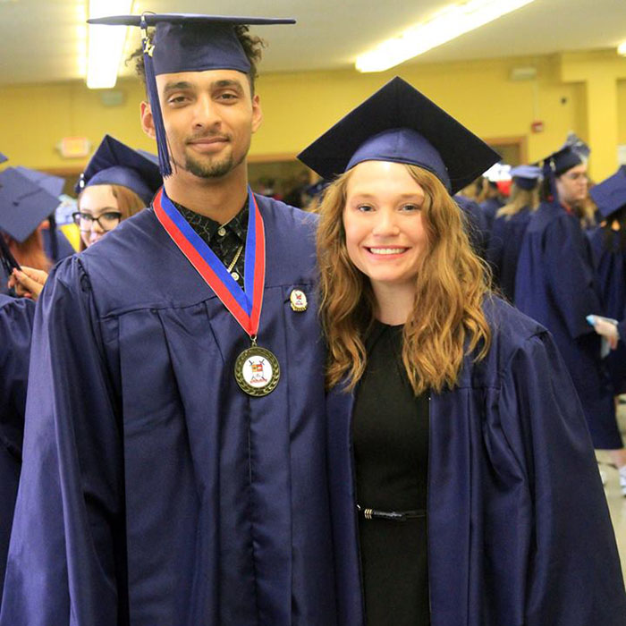 male and female students in cap and gown posing for photo after graduation.