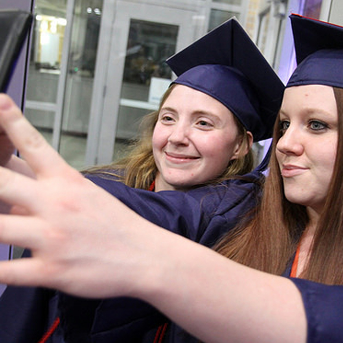 two women in cap and gown taking a selfie.