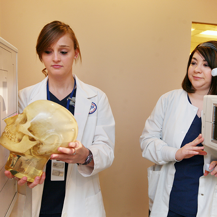 two female students in a x-ray room. one woman is holding a skull.