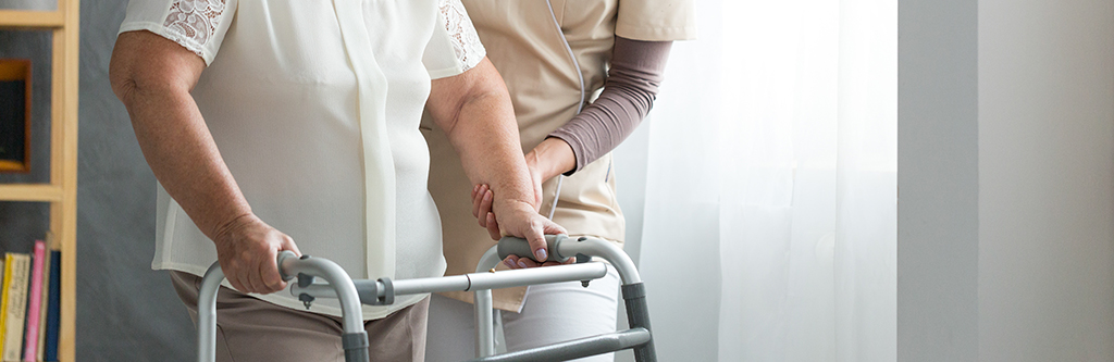 health care worker helping elderly women with a walker.