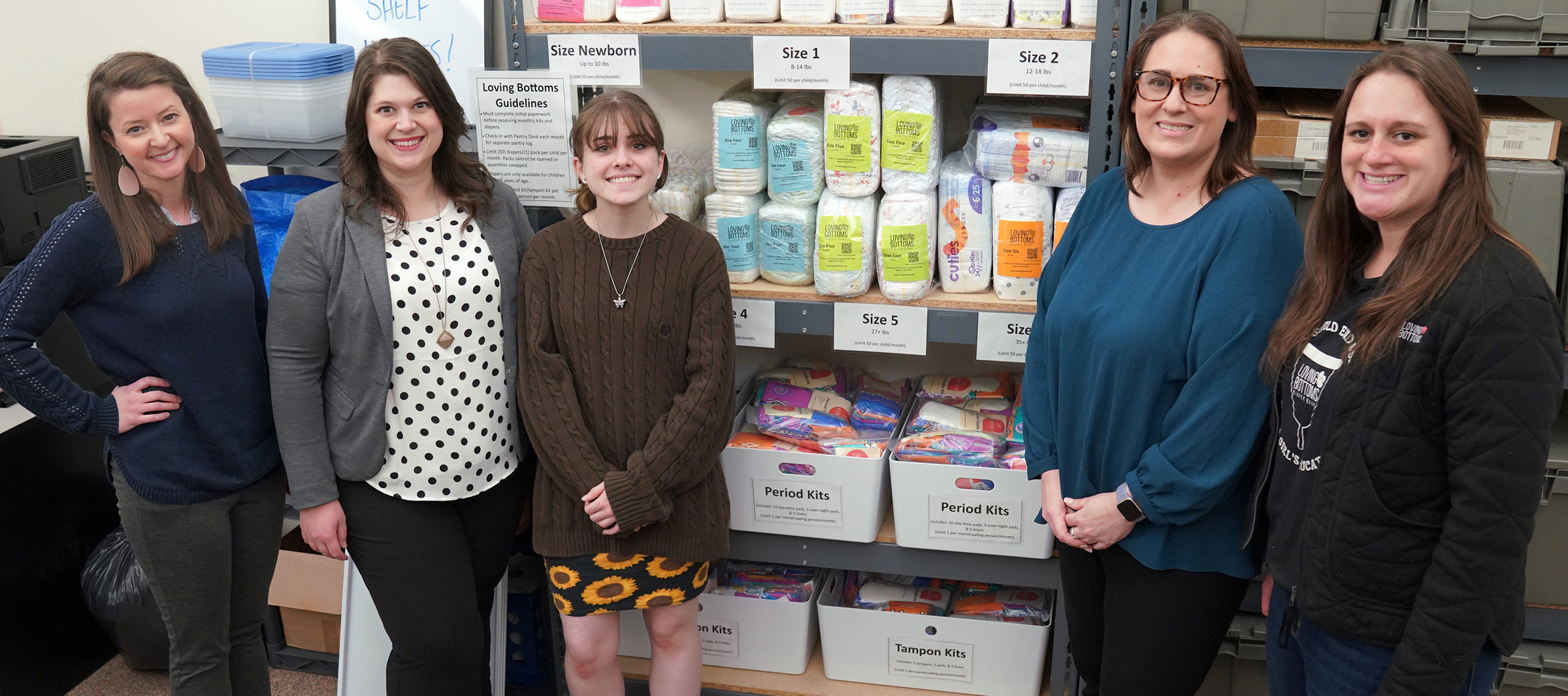 Autumn Scott, Carl Sandburg College associate vice president of academic planning; Genny Stevens, student life coordinator; student Samantha Cozad; Lee Ann Porter, Loving Bottoms Diaper Bank founder and executive director; and Loving Bottoms program coordinator Jenny Dowsey stand for a photo in front of Sandburg’s stock of feminine products, diapers and wipes in its Resource Room Campus Food Pantry.