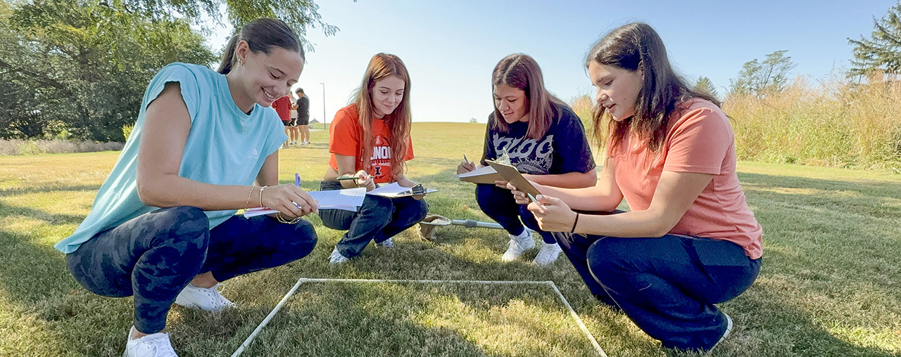 Four female students crouching around a PVC square for a biology class.