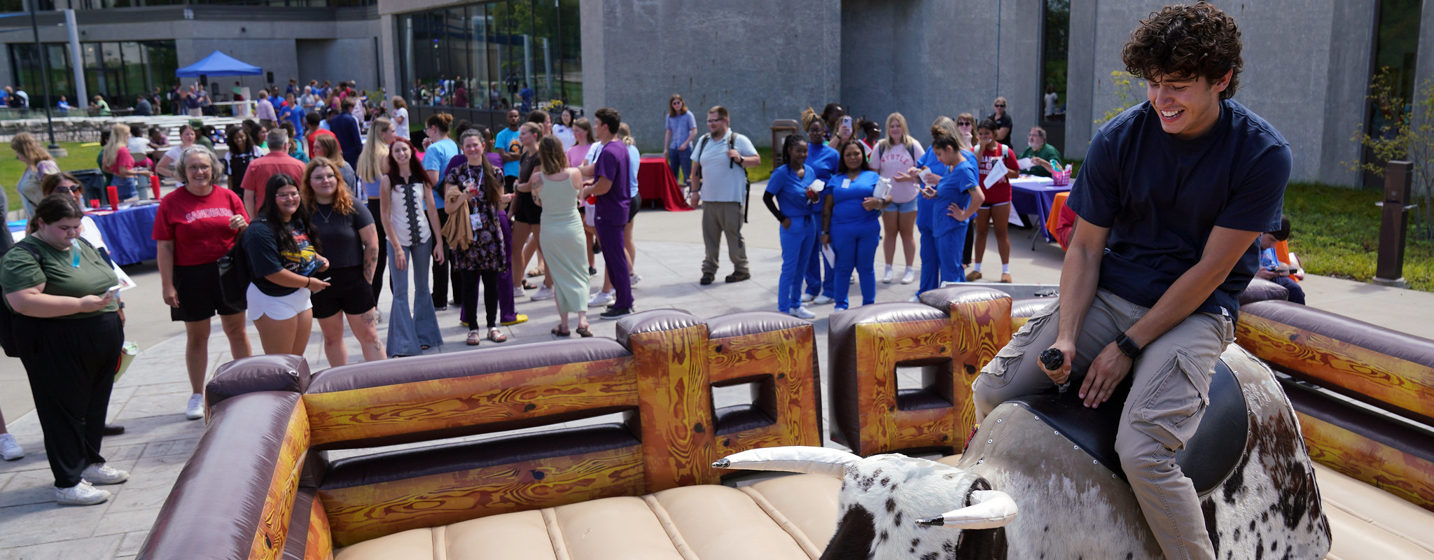 male student riding a mechanical bull at spring fest.