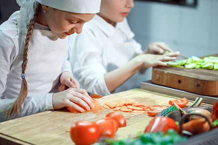 Two girls cutting vegetables in am kitchen.