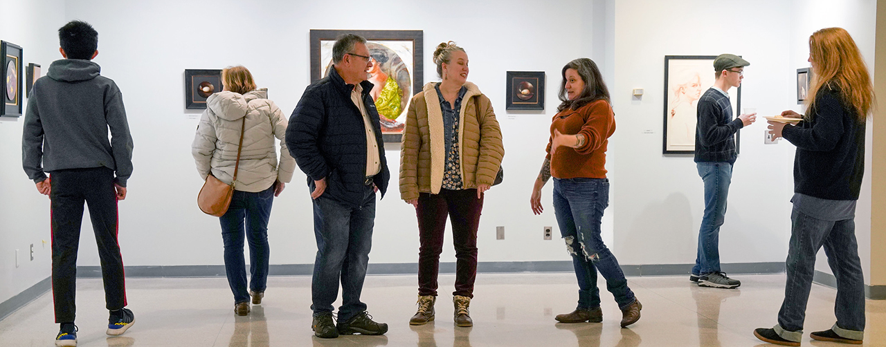 People in art gallery looking at paintings on the wall.