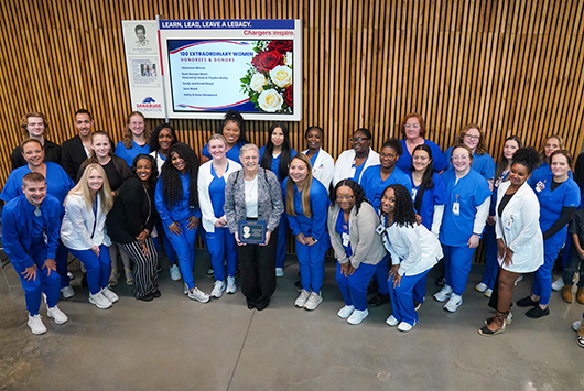 Nursing students in front of Ann Rhykerd-Asplund & 100 Extraordinary Women display.