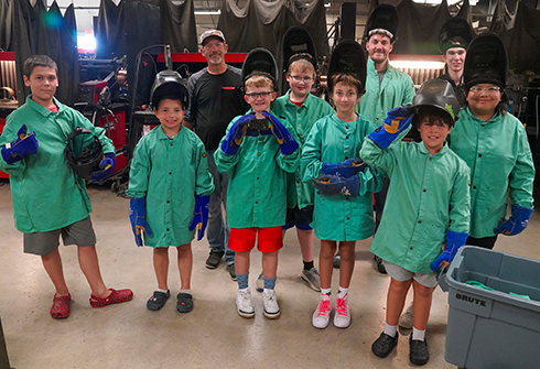 Kids on Campus participants in welding jackets and helmets.