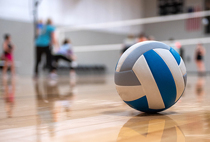 A volleyball sitting on the ground with kids playing in the background.