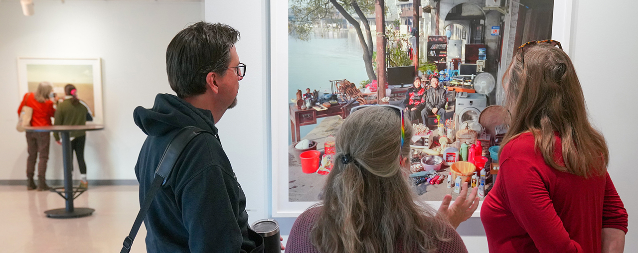 Three people looking at a photo of two people with all of their possessions around them.