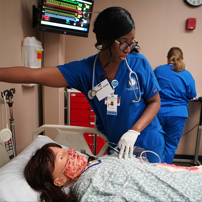 nursing student in nursing lab standing over virtual patient.